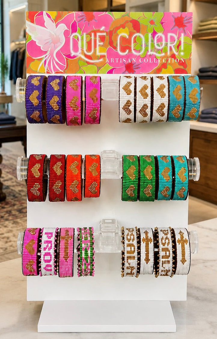 Display of colorful bracelets on a stand with Que Color branding in a boutique setting.
